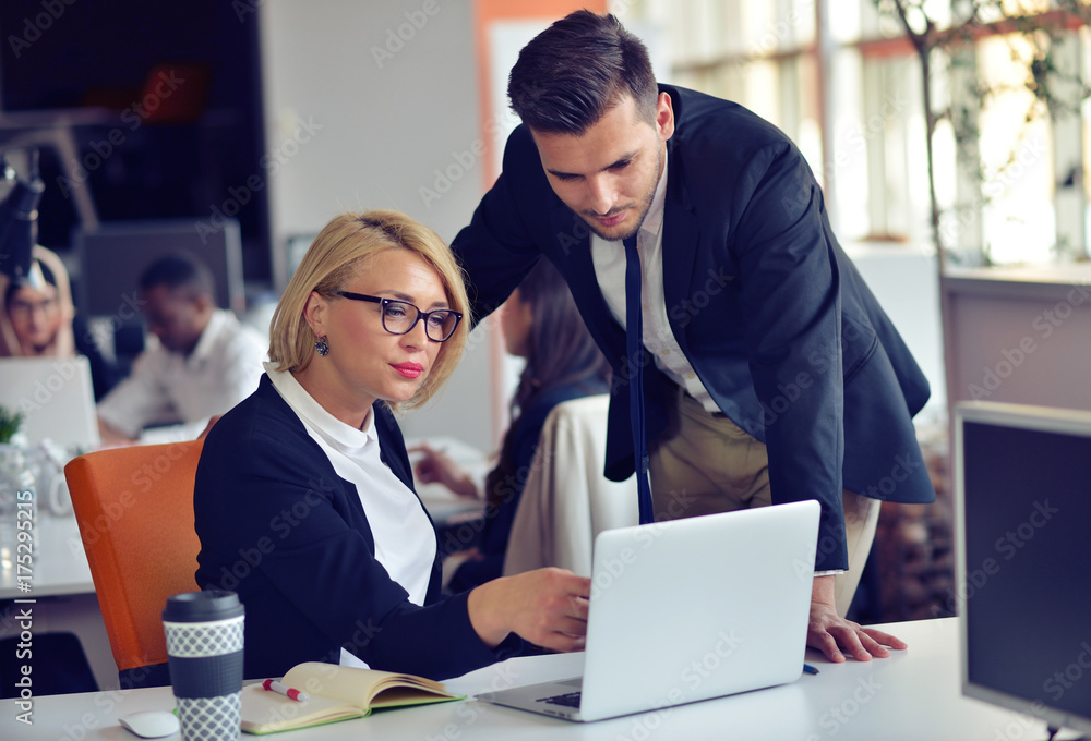 Beautiful young business partners are using a laptop, discussing documents and smiling while working in office. Beautiful young business partners are using a laptop, discussing documents and smiling while working in office.