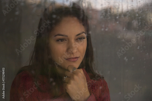 Beautiful woman is looking through the window on a rainy day.