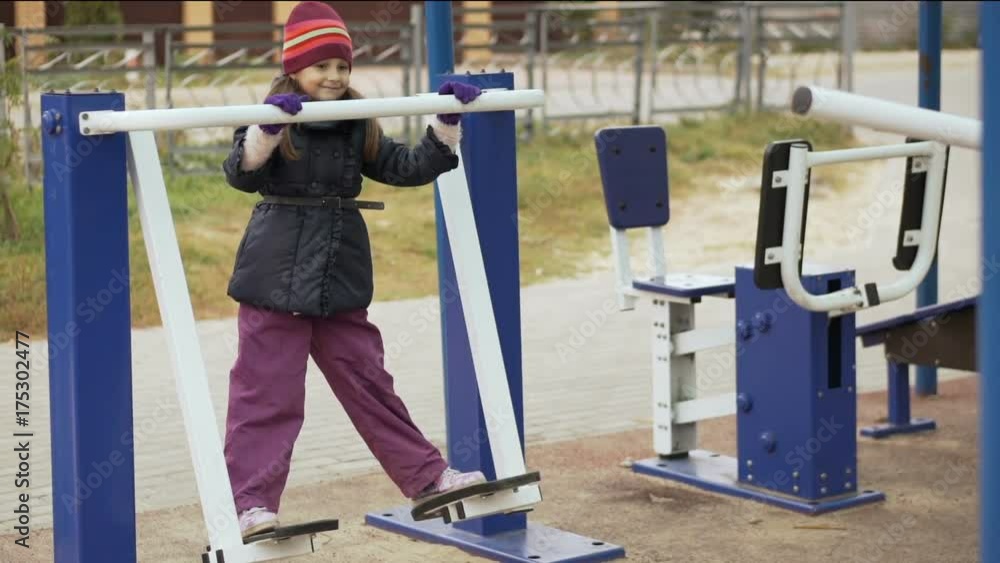 Little cute girl on the simulator for training of feet on the sportsground in the autumn time. Slow motion. Little cute girl on the simulator for training of feet on the sportsground in the autumn time. Slow motion.