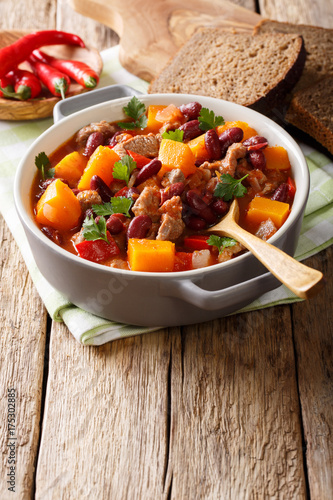 Stew with beef, pumpkin, red beans, tomatoes and chilli close-up in a pot. vertical