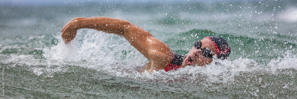 Triathlete man swimming freestyle crawl in ocean panorama banner. Male triathlon swimmer swimming in professional triathlon suit training for ironman on Hawaii.