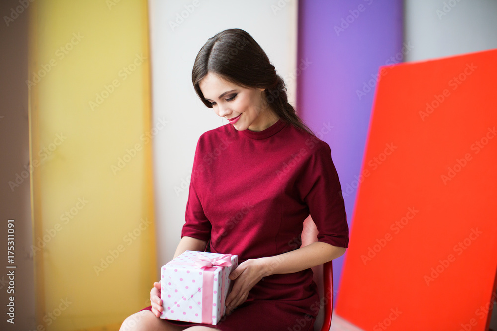 Fototapeta premium Beautiful woman in a burgundy dress holding a gift box.