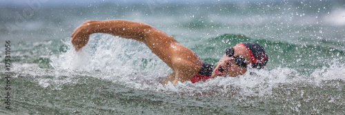 Triathlete man swimming freestyle crawl in ocean panorama banner. Male triathlon swimmer swimming in professional triathlon suit training for ironman on Hawaii.