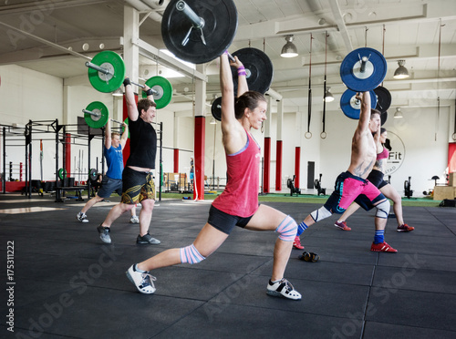 Flexible Athletes Exercising With Barbells In Gym