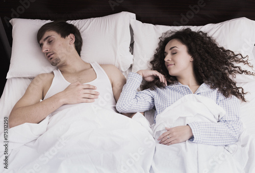 Young spouses sleeping tight in bed