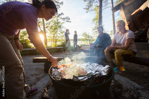 Woman Grilling Food On Skewers With Friends In Background