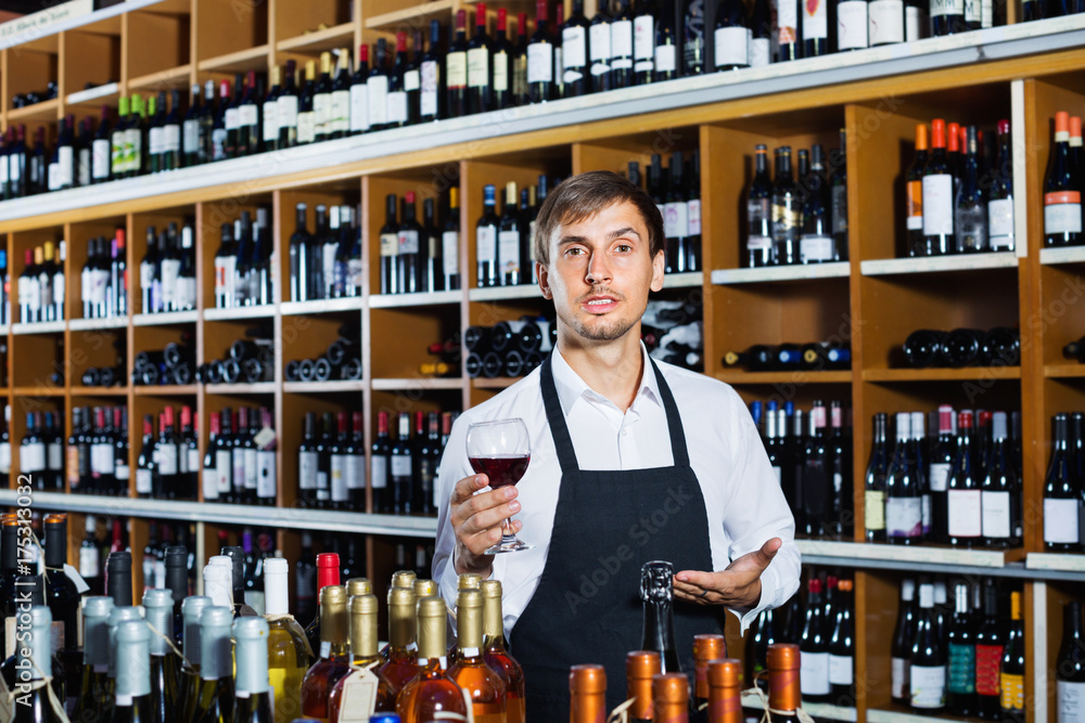 Seller man wearing apron suggesting to try glass of wine
