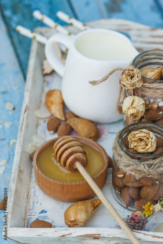 Honey in the wooden bowl, almonds and jar with milk on the wooden tray