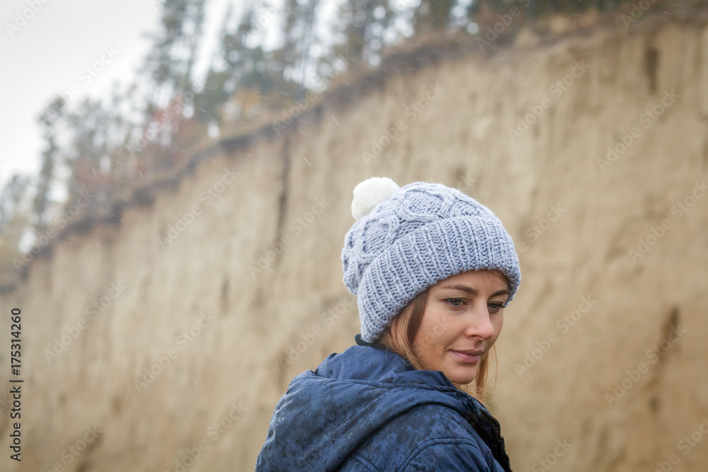 Close-up A young dark-haired woman in a knitted gray cap made of natural wool, a blue jacket on a warm autumn day against the backdrop of a sand pit and coniferous forest Close-up A young dark-haired woman in a knitted gray cap made of natural wool, a blue jacket on a warm autumn day against the backdrop of a sand pit and coniferous forest