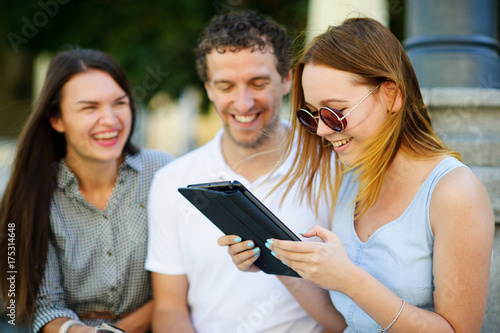 Two girls and the guy with interest look at the tablet screen.