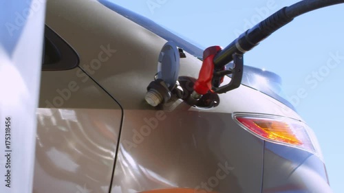 Tracking shot shot of male hand inserting fuel nozzle into opened car tank at gas station at sunny day photo