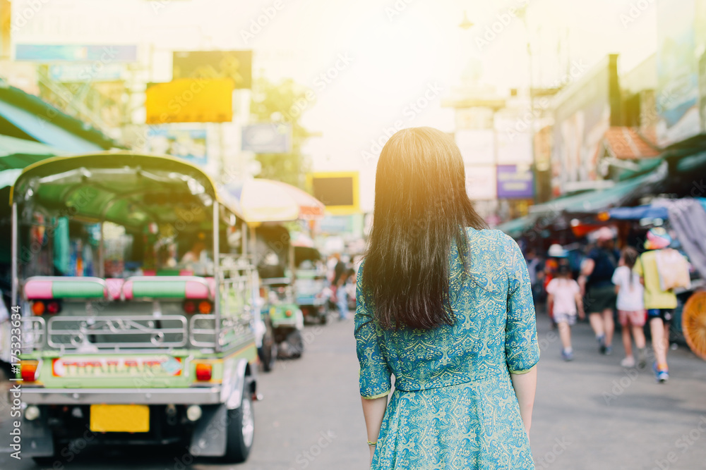 Woman in traditional Asian dress on Khaosan road with tuk tuk taxi behind, appreciating Thai local culture - travel and local life concept