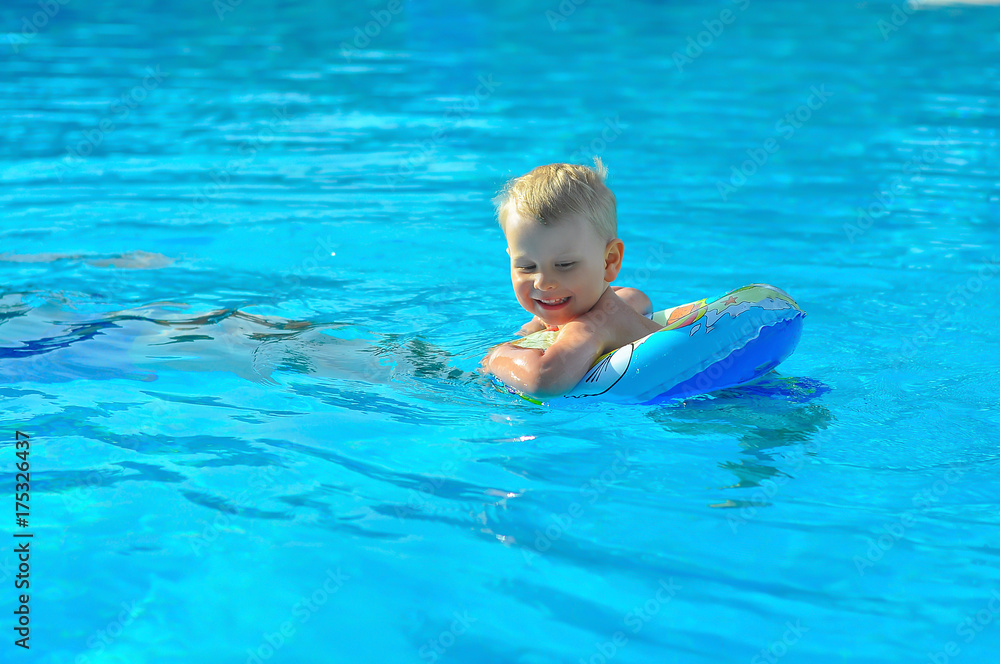 the little blonde boy of three years swim with swimming ring in an indoor pool