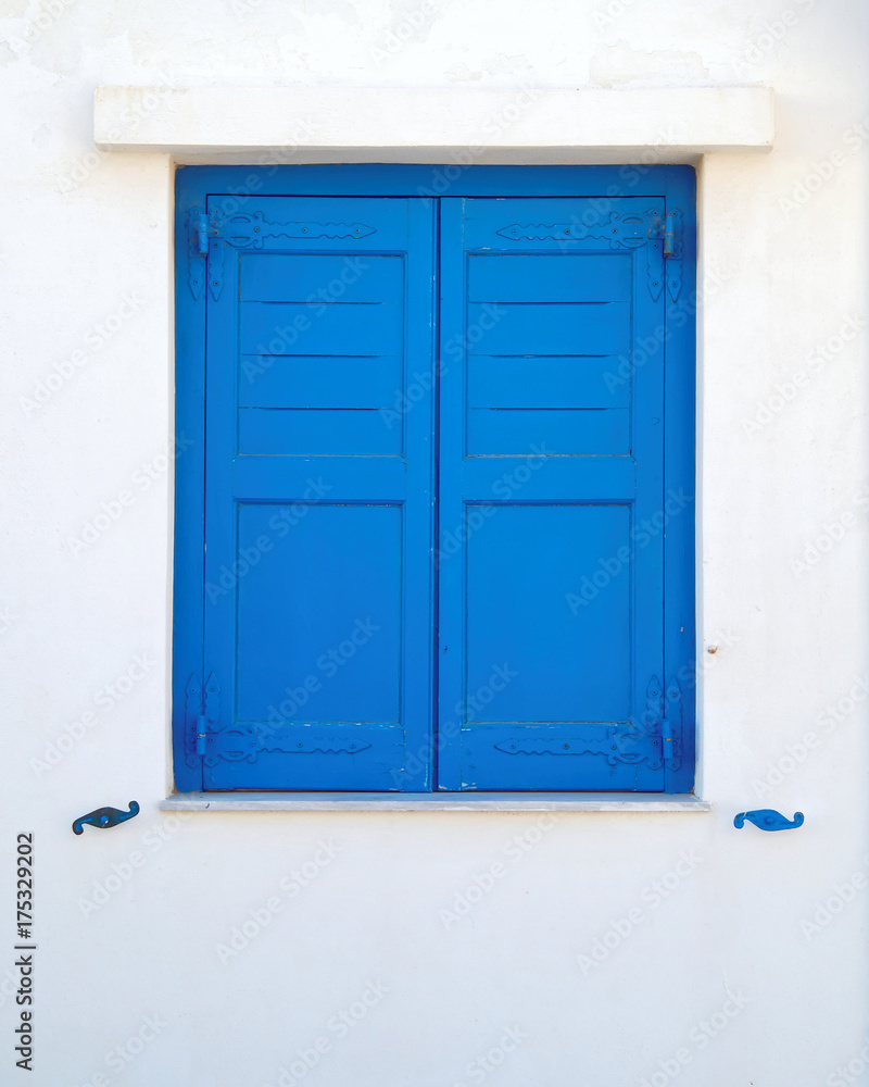 Greece, blue painted wooden window shutters on white wall