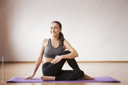 Beautiful and healthy young sporty woman in sportswear doing yoga in light room on mat