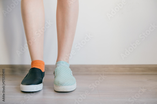 Female naked legs standing on wooden floor in front of white wall. Women`s feet in different leather shoes. Missmatched socks. Odd unusual weird unrecognizable bizarre kinky girl. Soft taned skin.