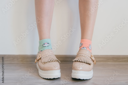 Naked women`s feet in feminine business bright leather shoes with tankette and white sole standing at home. Female feet in missmatched cotton colorful socks. Innocence and youth lifestyle. Odd girl.