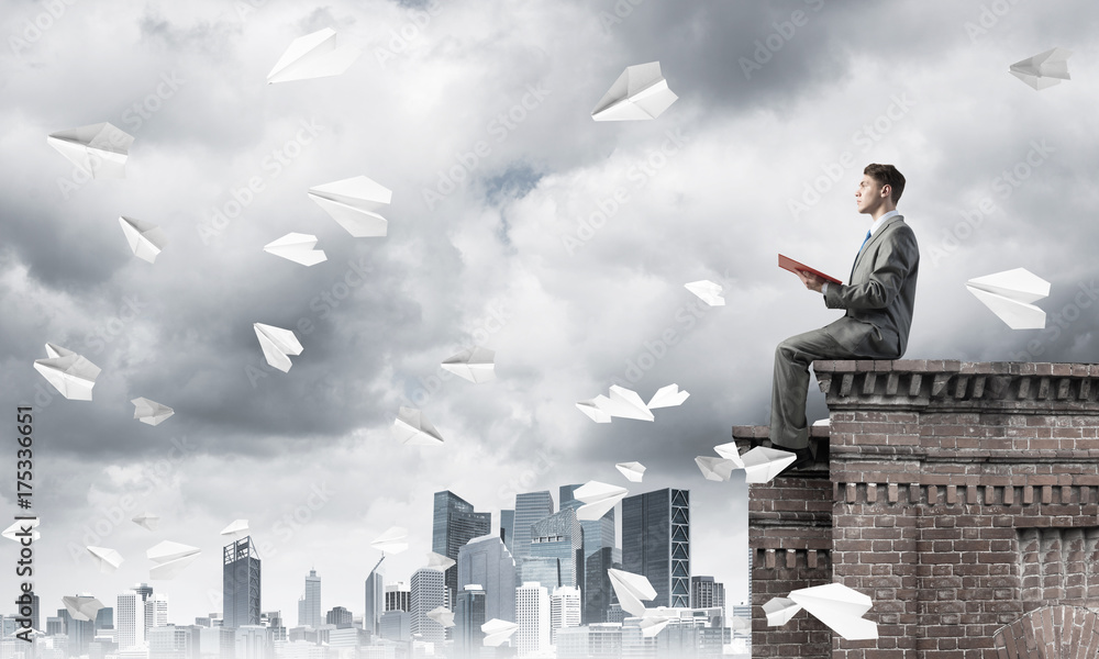 Man on roof edge reading book and cityscape at background Man on roof edge reading book and cityscape at background