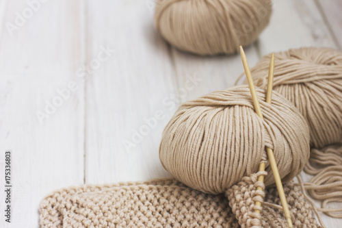 Beige Merino yarn with bamboo needles on white wooden background