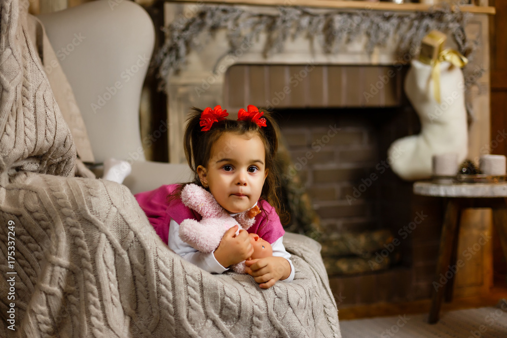 Fototapeta premium Little girl near fireplace holding soft toy in hand.