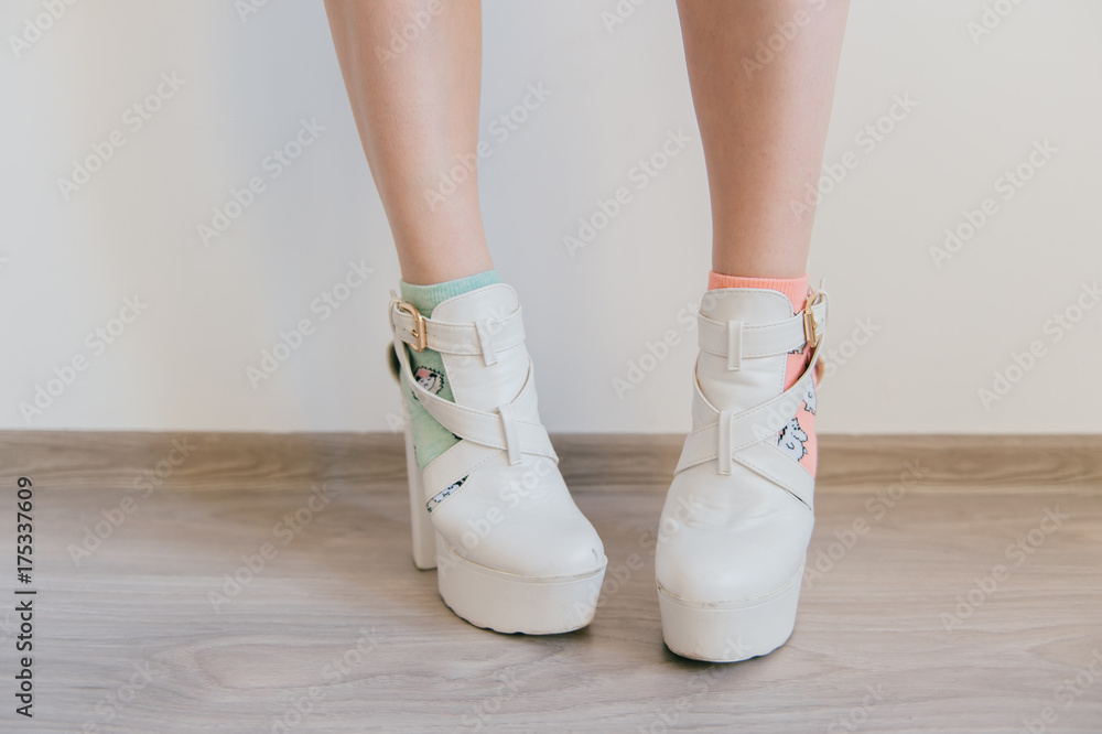 Kinky women`s legs in missmatched colorful cotton socks on white background. Female feet in eccentric white leather fashionable trend modern shoes on high heels. Unrecognizable impudent cocky teenager