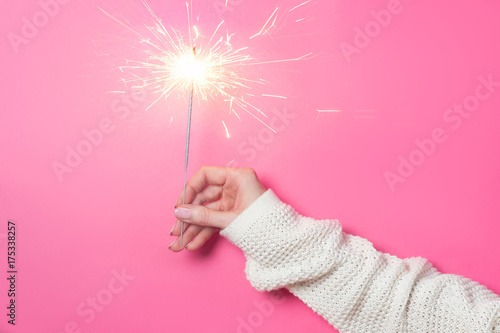 Sparkling Bengal fire in a woman's hand on a pink background. Christmas Concept