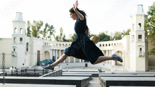 Girl in black dress jumping at city