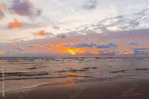 A pink, blue and purple creamy cloudy sunset, with sun rays breaking through the clouds. A relaxed quiet sunset evening on the coast.