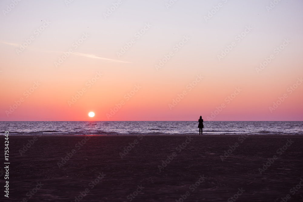 A vivid deep purple and pink los angeles sunset. A woman silhouette taking a walk on a relaxed quiet sunset evening on the coast.