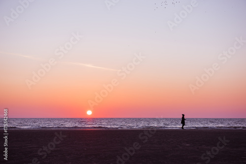 A vivid deep purple and pink los angeles sunset. A woman silhouette taking a walk on a relaxed quiet sunset evening on the coast.