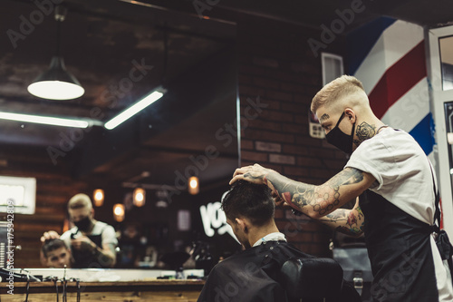 Photo Crop tattooed stylist concentrated on shaving man with machine doing hairstyle