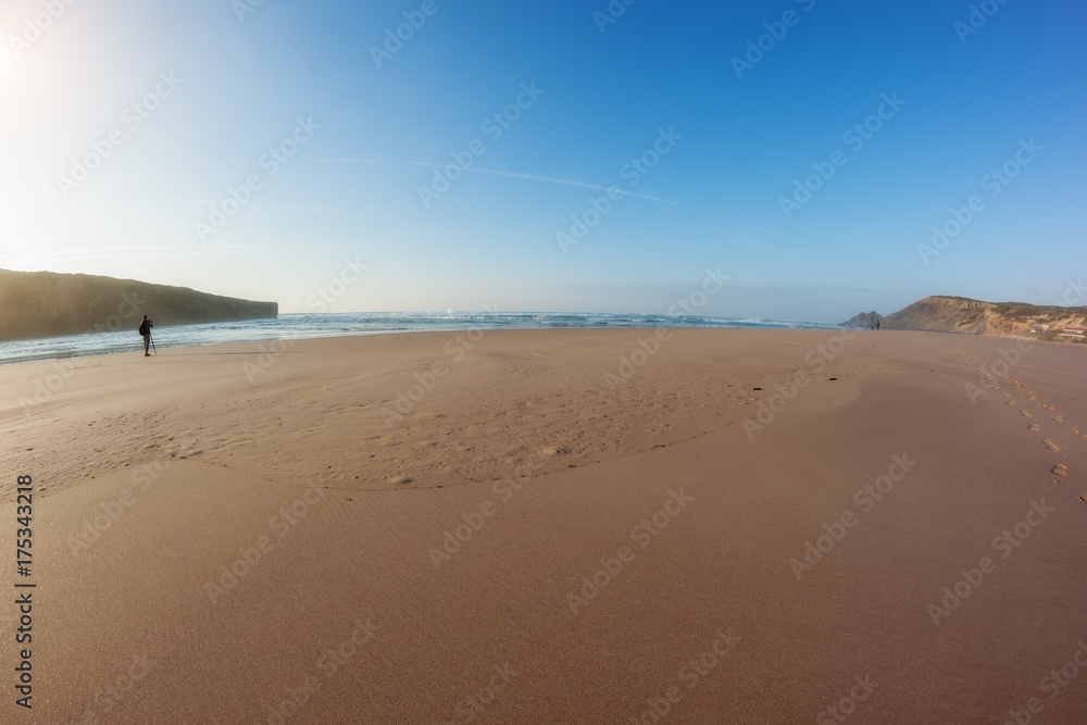 Panorama of a sandy beach and a photographer working in front of sea.