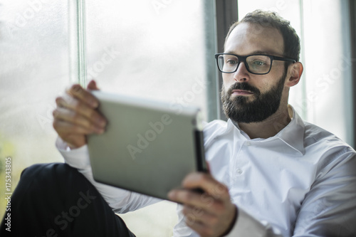 Businessman sitting by window, using digital tablet