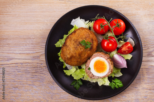 Scotch eggs on a plate with cherry tomatoes and salad. View from above, top studio shot, horizontal