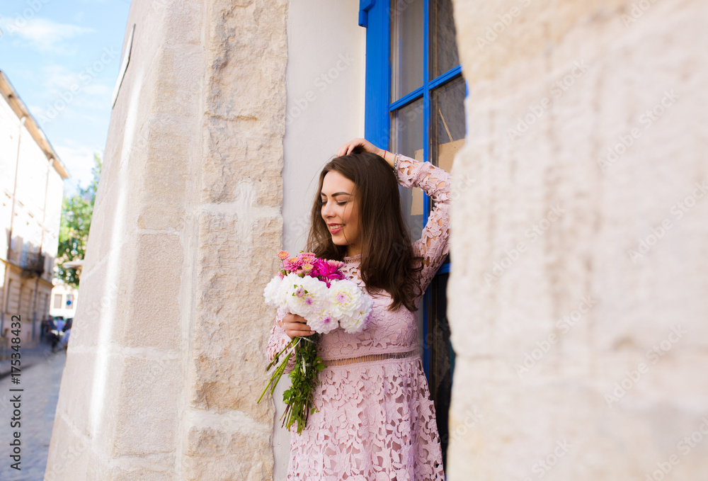 Happy brunette model in short dress holding bouquet of flowers at the city