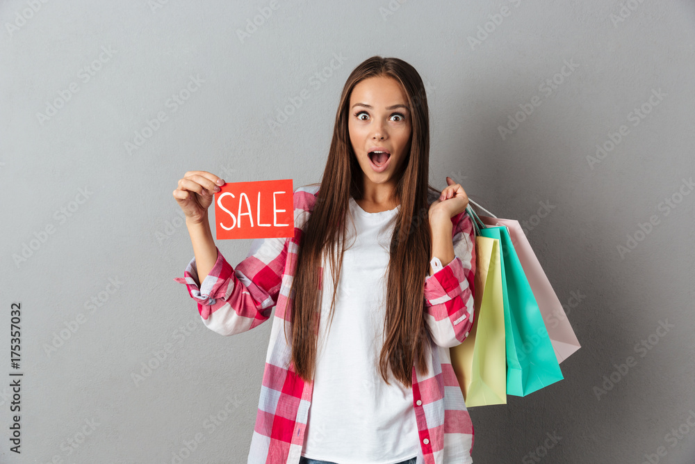 Amazed pretty caucasian woman holding sale sign and shopping bags, looking at camera Amazed pretty caucasian woman holding sale sign and shopping bags, looking at camera