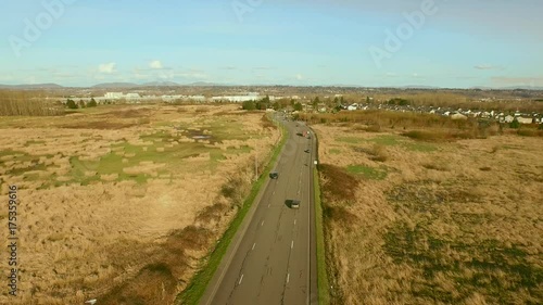 An aerial shot of a road with cars driving at sunset hour with warm and rich lighting, with a sweep motion camera movement, establishing shot