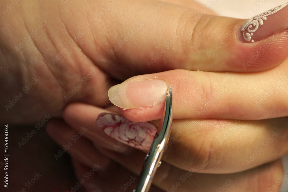 Fototapeta premium A student at the training courses of a manicure prepares the hand of a lady client with a manicure scissors for cuticles before applying shellac