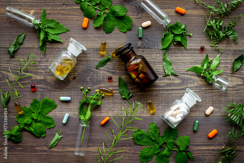 Herbal medicine pattern. Leaves, bottles and pills on wooden background top view
