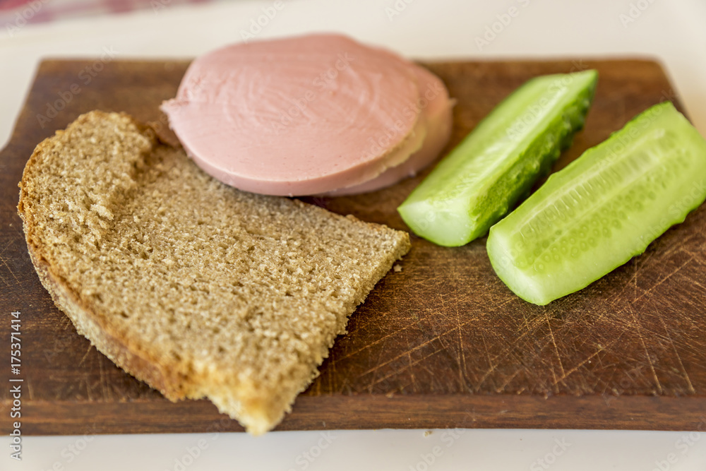 rye bread, cucumber and sausage on brown wooden desk rye bread, cucumber and sausage on brown wooden desk