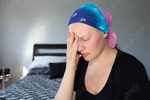 Young cancer patient in a headscarf rubs face with stress