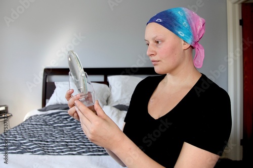 Young cancer patient in a headscarf looks at reflection in the mirror