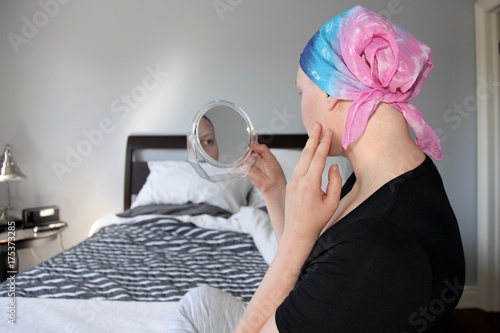 Young cancer patient in a headscarf looks at face in mirror