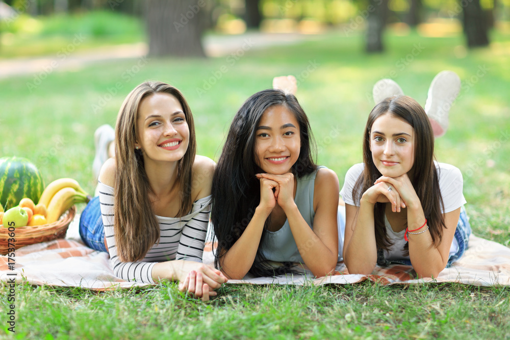 Three young happy multiracial women lying on grass in park Three young happy multiracial women lying on grass in park