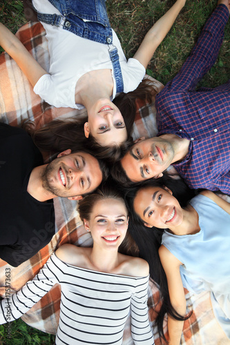 Five cheerful friends lying on grass top view portrait