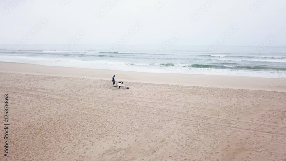 Young couple of friendly surfers wearing wetsuit holding surfboards, walking by the sea on a morning surfing session. Young couple of friendly surfers wearing wetsuit holding surfboards, walking by the sea on a morning surfing session.