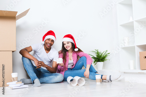Happy young couple in Santa hats in new house.