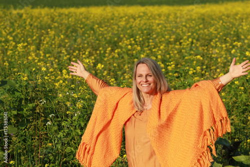 Happy mature woman with spread arms in flower field