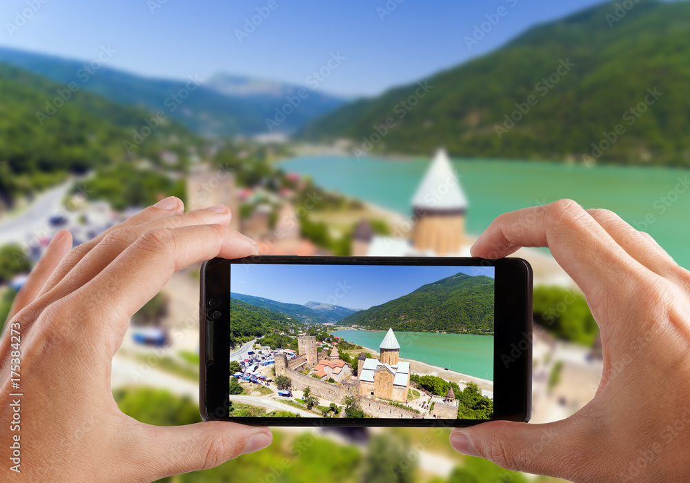 Travel concept. Hands making photo of Ananuri Castle with Church on the bank of lake, Georgia.