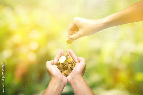 Male hand give and receive golden coins. Saving, money, finance donation, giving and bussiness concept. on green yellow nature bokeh background.